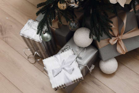 Bright silver gifts in packaging and with bows under the Christmas tree on the floor. Christmas...