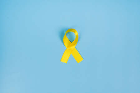 Yellow gold ribbon on a yellow background. Children cancer concept. Awareness month. Childhood...