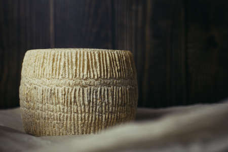 Maasdam cheese head on a background of dark wooden boards and parchment paper. Hard goat cheese on a...