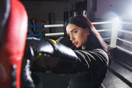 A beautiful girl in boxing gloves hits her paws in the ring. Sexy woman is training in the gym. Beautiful brunette is engaged in boxing.の写真素材