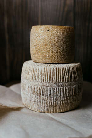 Different homemade cheeses on a dark wooden background. Pieces and cheese heads of kravot, manchego,...