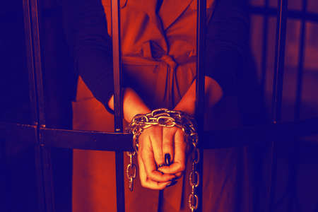 Woman behind bars. Female crime concept. Girl's hands tied with chains, domestic violence.