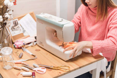 Seamstress works on a sewing machine. The girl sews and holds a pink cloth.の写真素材