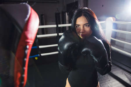 A beautiful girl in boxing gloves hits her paws in the ring. Sexy woman is training in the gym. Beautiful brunette is engaged in boxing.の写真素材