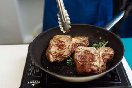Raw Fresh Marbled Meat Beef on a grill pan ready for cooking. Man cooking beef steaks. Male hands holding a grill pan with beef steaks on kitchen.の写真素材