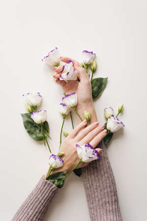 Delicate hands and spring flowers of eustoma are on the white table. the concept of skin care. Natural cosmetics for hand skin care, a means to reduce wrinkles on the hands, moisturizing. Natural flower extract cosmetics, beauty and fashion.の写真素材