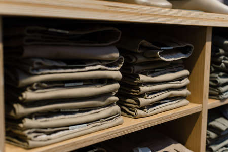 pile of beige jeans on a shop window in the store. Folded jeans are on the shelf. A stack of classic...