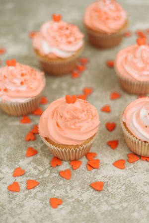Pink cupcakes on a gray background for Valentine's day. Gift sweets with cream and sprinkle with hearts.の写真素材