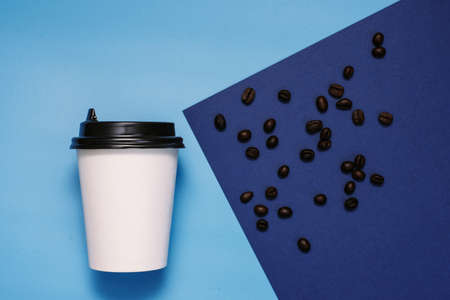 White cardboard glass with a plastic black lid on a blue and cyan background with coffee beans. Glass with take-away coffee. The trend color is classic blue. Copyspace, flat lay.の写真素材