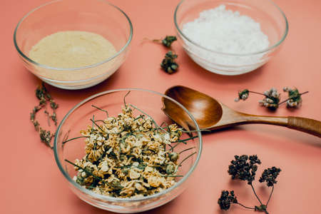 Dried chamomile in a glass bowl on a background of sea salt and yellow clay, natural powder. Create soothing and moisturizing cosmetics in a mortar at home. A natural skin care recipe.の写真素材