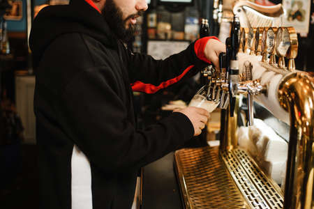 barman pouring beer in a bar. Bearded courageous man pours you a foaming drink.の写真素材