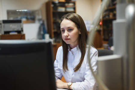 Young scientist works in modern biological lab. Happy young female researcher working at desk using computer in the laboratory.の写真素材