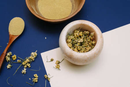Marble mortar with dried chamomile for natural cosmetics. Clay and glass bowls with yellow powder or clay and flowers. Flat lay, classic blue.の写真素材