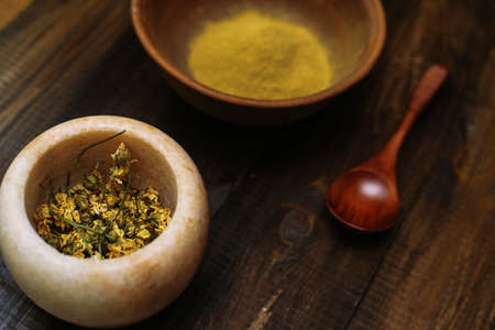 Marble mortar with dried chamomile for natural cosmetics. Clay bowl with yellow powder or clay and flowers on a wooden background. Flat lay.の写真素材