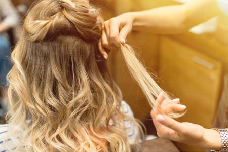 The hairdresser creates curls and wavy hair in the blonde. Hands of the hairdresser curls curls at the client.の写真素材
