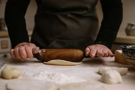 A woman rolls dough for dumplings and convenience foods, baking with a dark wooden rolling pin. The cook makes the dough.の写真素材