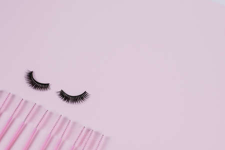 Black fake ribbon eyelashes and brushes for combing extension eyelashes on a pink trendy pastel...