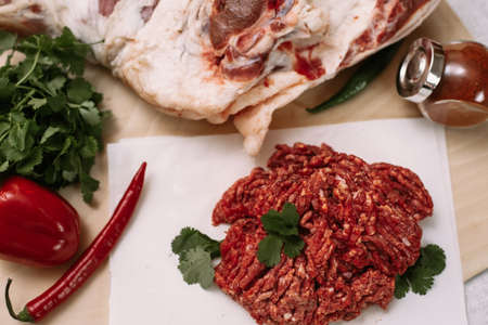 Red fresh minced meat on the background of lamb legs, red pepper and greens. Ground beef on the...