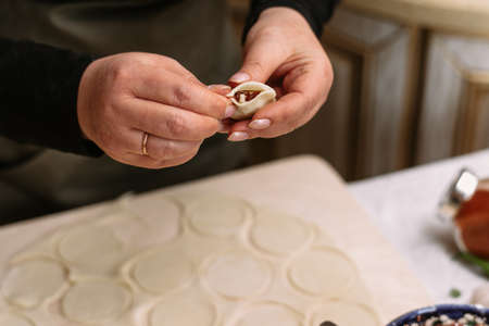 A woman in the kitchen sculpts homemade dumplings or semi-finished products. The cook wraps the minced meat from beef into the dough.の写真素材