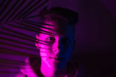 A young guy with a palm leaf in neon light looks at the camera. Trend photo of a teenager.の写真素材