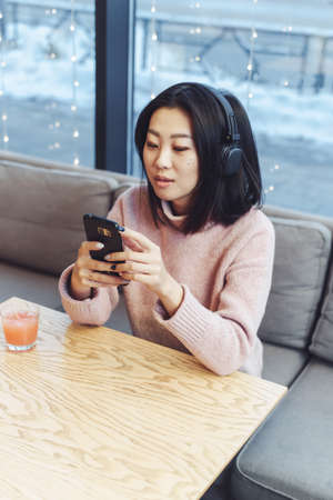 Asian girl alone in the city sits in a cafe and listens to music. Enjoying music in a public place.