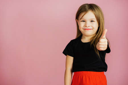 Little girl shows thumb up on a pink background. Template for your advertisement. Funny shot of...