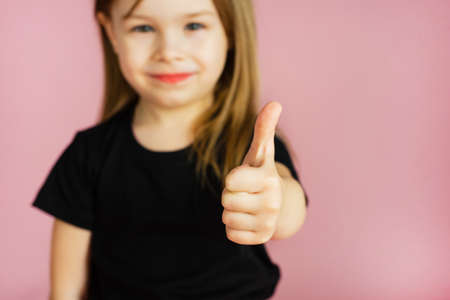 Little girl shows thumb up on a pink background. Template for your advertisement.の写真素材