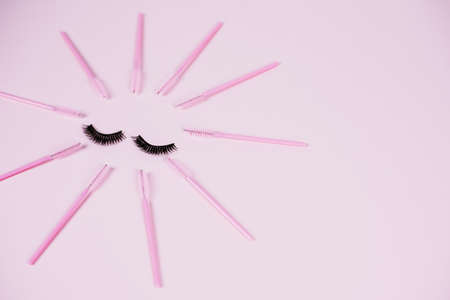 Black fake ribbon eyelashes and brushes for combing extension eyelashes on a pink trendy pastel background. False eyelashes, applicator and brushes. Top view, flat lay.の写真素材