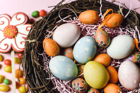 Painted and decorative eggs for the Easter holiday in a nest of branches next to sweets and...