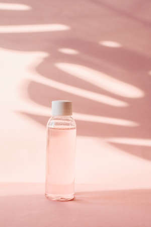 Plastic bottle with pink rose water on a pastel background with tropical shadow of a palm leaf. Transparent toner and toner to moisturize and cleanse the skin. Micellar water or cleansing foam.の写真素材