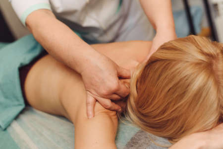 Young blonde woman receiving a back massage in a medical center. Female patient is receiving treatment by professional therapist with beautiful hands.の写真素材