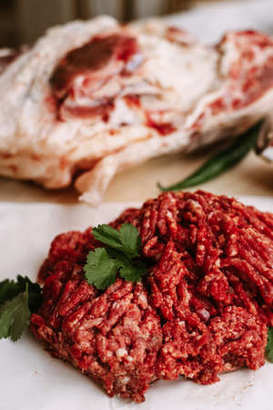 Red fresh minced meat on the background of lamb legs, red pepper and greens. Ground beef on the background of fresh meat in the kitchen of a housewife.の写真素材