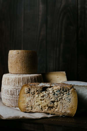 Different homemade cheeses on a dark wooden background. Pieces and cheese heads of Gorgonzola,...