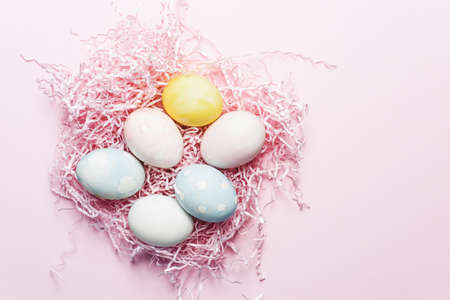 Painted eggs in pastel colors on a pink paper filler and background. Modern easter holiday template.