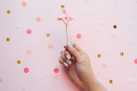 Children's pastel weather vane topper for a cupcake in the hand of a girl with manicure on a pink background with confetti. Birthday festive background.の写真素材
