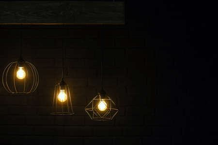 Orange retro lamps hanging on a wooden board on a background of dark black brick wall. Modern...