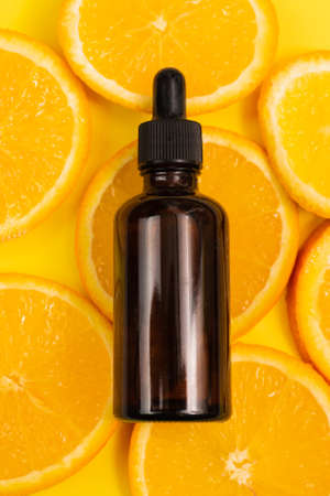 Citrus fruit essential oil, vitamin c serum, beauty care aroma therapy. Natural vitamin c serum, skincare, essential oil products. Cosmetic brown glass vial with dropper and fresh juicy orange fruit slice on orange background.の写真素材