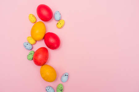 Easter colored eggs on a pink background. Red and yellow chicken eggs with pastel quail eggs. Easter...