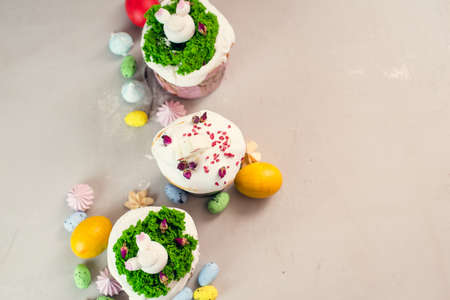 Orthodox Easter cakes decorated with cream in the form of grass and rabbit figurines made of white chocolate on a gray background next to painted eggs. Easter food concept. Idea for kids.の写真素材