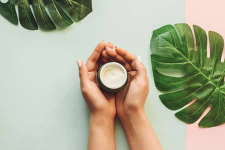 Girl holds moisturizer in her hands on a background of fresh palm leaves. The concept of natural cosmetics made from tropical ingredients.の写真素材