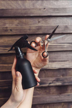 Hairdresser tools on a wooden background in the hands of a master. Protective spray and hair scissors. Professional hairdresser tools.の写真素材