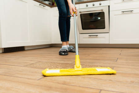 Worth housewife cleaning floor at home. Lovely woman washes wooden floors from a laminate in a bright kitchen.の写真素材