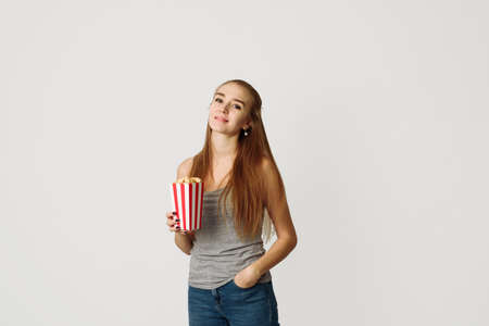 Portrait of a laughing girl in casual clothes holding popcorn box and looking at camera isolated...