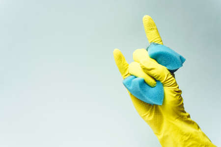 yellow rubber glove is holding sponge on the white background. yellow rubber glove is showing rock...