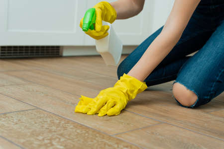 A girl is washing a floor in yellow gloves. A girl is cleaning a room with detergents.