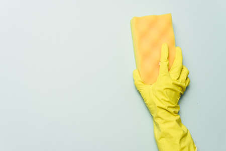 yellow rubber glove is holding sponge on the bluebackground. yellow rubber glove is cleaning with...