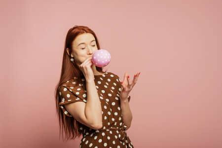 A redhead girl is inflating the balloon. A girl with balloon. A girl with opened-eyes is blowing.の写真素材