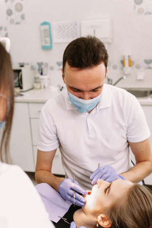A beautiful woman lies in the dentists chair. The doctor and assistant are treating the patients...