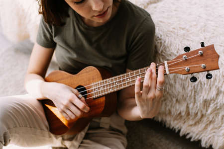 A beautiful woman plays the little guitar at home. A young girl plays ukulele during self-isolation.の写真素材