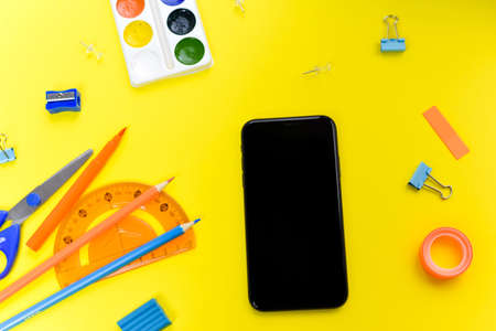 Office supplies near the phone on a yellow background. The concept of electronic distance learning.